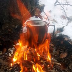 a pot sitting on top of a fire in the middle of snow covered ground next to trees