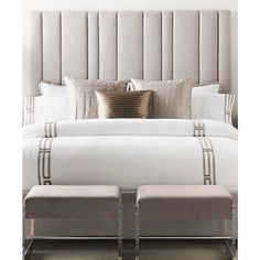 a large bed with white sheets and pillows on it's headboard, sitting next to two stools