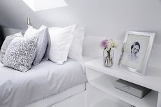 a white bed topped with lots of pillows next to a night stand and framed pictures