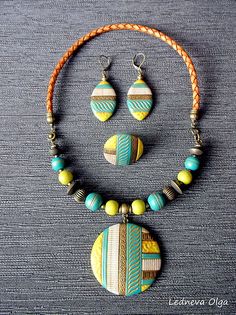 a necklace and earring set with two pendants on a gray surface, next to an orange cord