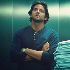 a man is standing in front of stacks of folded blue shirts with his arms crossed