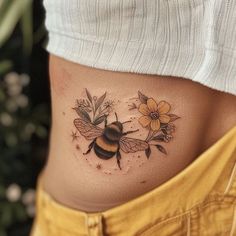 a woman's stomach with a bee and flowers tattoo on her lower side belly