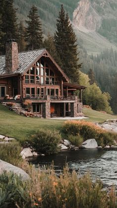 a log cabin sits on the edge of a mountain stream in front of a house