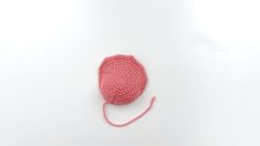 a pink crocheted object on a white surface with a red string attached to it