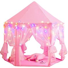 a pink tent with fairy lights on the top and curtains around it, is set up in front of a white background