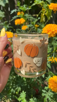 a woman holding up a glass with pumpkins painted on it and flowers in the background