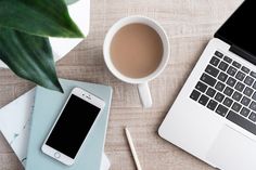 an open laptop computer sitting on top of a wooden desk next to a cup of coffee