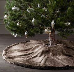 a christmas tree with ornaments on it and a rug in front of the trees trunk