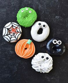 four decorated donuts sitting on top of a black surface with fake eyes and faces