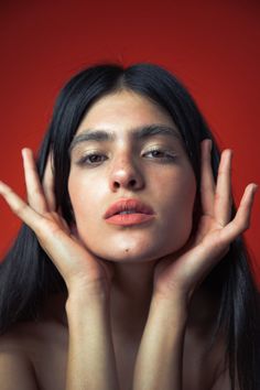 a woman with her hands on her face and eyes closed, posing in front of a red background