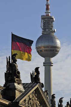 the german flag is flying on top of an old building with a spire in the background