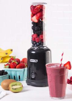 a blender filled with berries and kiwis on top of a table next to bowls of fruit