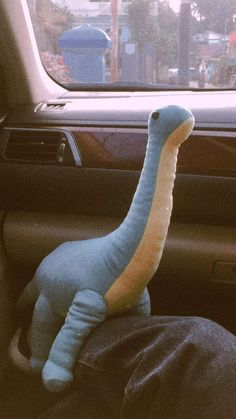 a stuffed dinosaur sitting in the driver's seat of a car