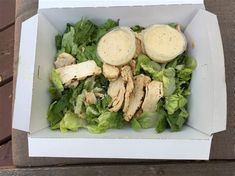 a white box filled with lettuce and sliced chicken on top of a wooden table