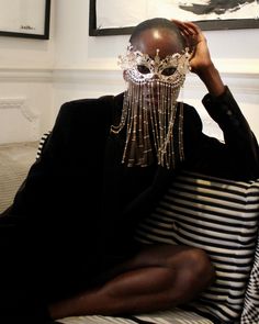 a woman sitting on top of a couch wearing a mask and beaded headdress