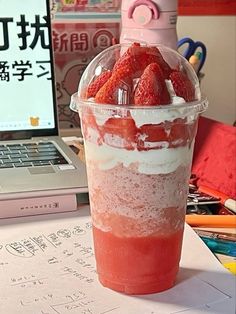 a cup filled with strawberries sitting on top of a table next to a laptop