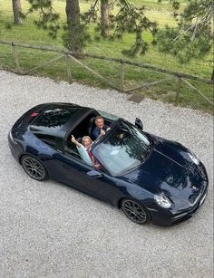 two people sitting in the drivers seat of a black sports car