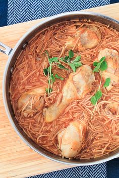 a pan filled with chicken and noodles on top of a wooden table next to a blue towel