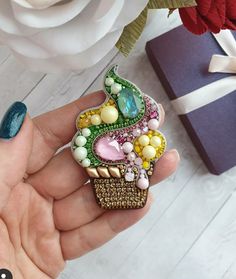 a person holding a colorful brooch in their hand next to a gift box and flower