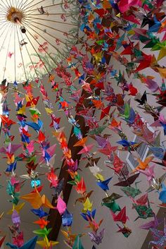 colorful origami cranes are hanging from the ceiling in front of an umbrella that is upside down