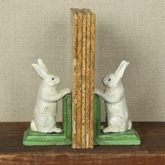 two white rabbits sitting on top of a green bookends next to each other