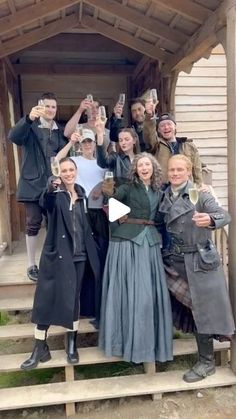 a group of people standing on steps holding wine glasses in front of a wooden structure