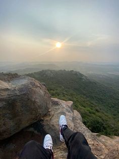 someone is sitting on top of a large rock with their feet up in the air