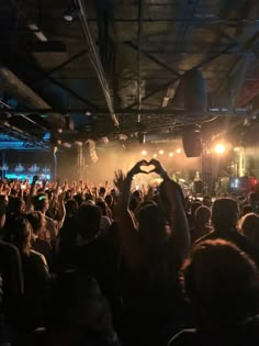 a large group of people at a concert with their hands in the shape of a heart