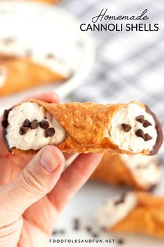 someone is holding up a piece of bread with cream and chocolate chips on it in front of other pastries