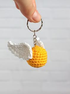 a hand holding a crocheted keychain with an angel wing on it