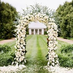 a wedding arch with white flowers and greenery in front of a large house on the lawn