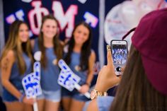 a group of young women standing next to each other in front of a wall holding up cell phones