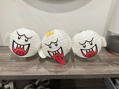 three paper lanterns with faces painted on them, one is white and the other has red tongues