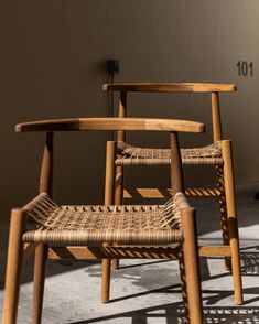 two wooden chairs sitting next to each other on top of a cement floor in front of a wall