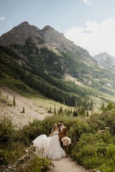 a bride and groom walking down a path in the mountains