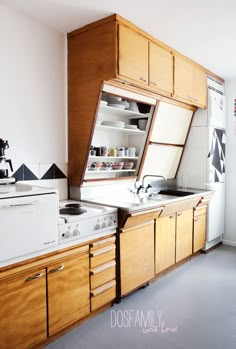 a woman standing in front of a stove top oven next to wooden cabinets and drawers