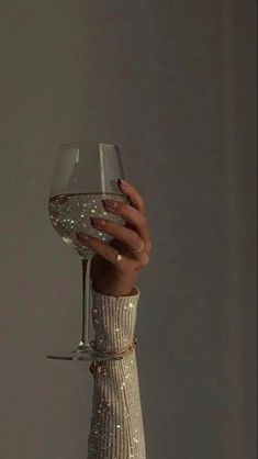 a woman holding a wine glass in her right hand and wearing a white dress with sequins on it