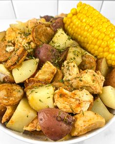 a white bowl filled with potatoes, corn on the cob and other food items