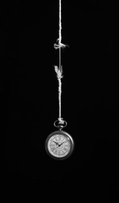 a clock hanging from a rope in the dark