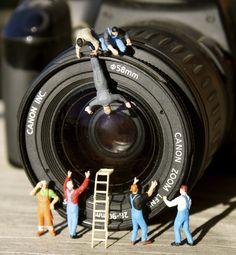 small figurines are placed on top of a camera with the lens in view