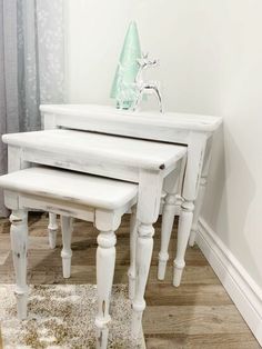 three white tables sitting on top of a wooden floor next to a window with curtains