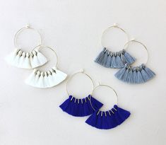 three pairs of tasseled hoop earrings hanging from hooks on a white wall background