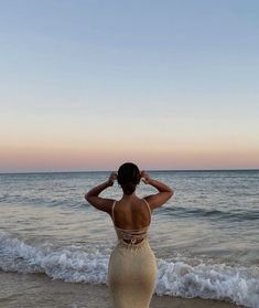 a woman standing on top of a sandy beach next to the ocean with her hands in her hair