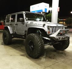 a silver jeep parked in front of a gas station at night with its lights on