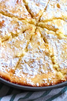 a cake with powdered sugar on top is sitting in a black pan next to a green and white striped towel