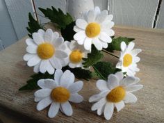 three white and yellow flowers sitting on top of a wooden table