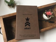 an army book sitting on top of a wooden tray next to a flower pot and pen