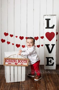 a little boy sitting on top of a wooden crate in front of a sign that says i love kissing booth