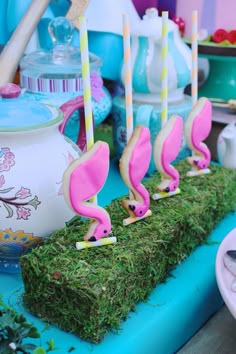 some pink flamingos are sitting in the grass with teapots and cups behind them