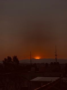 the sun is setting in the sky over some rooftops and buildings, with mountains in the background